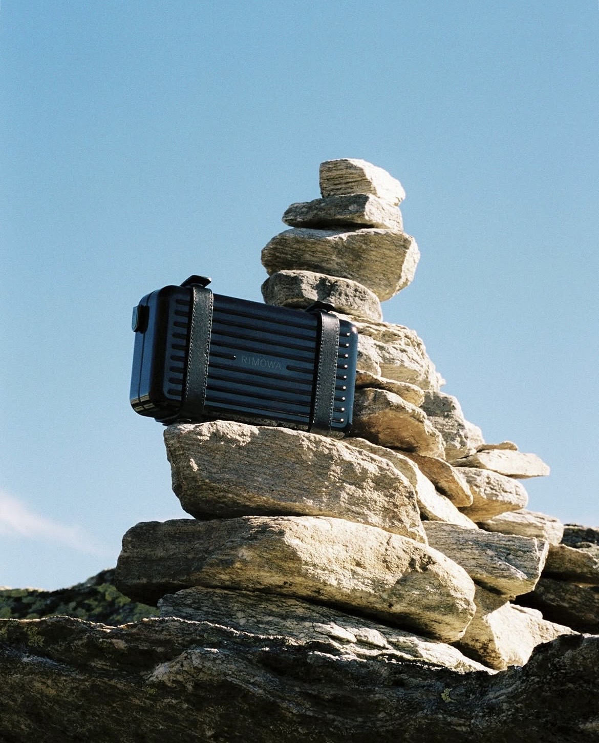 Maleta RIMOWA negra junto a unas rocas durante un viaje
